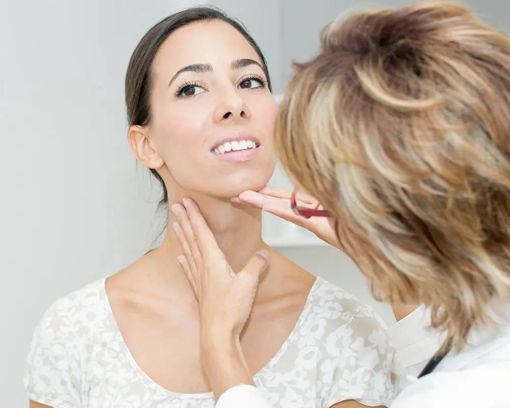 A woman looking in the mirror while holding her neck.