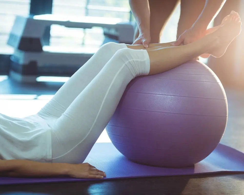 A person is sitting on the floor with their feet on an exercise ball.